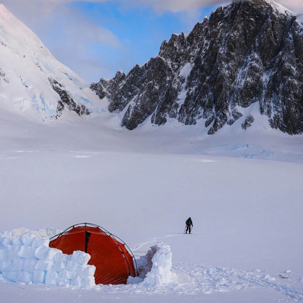 Red tent with a small snow wall in a snowy mountain landscape. 