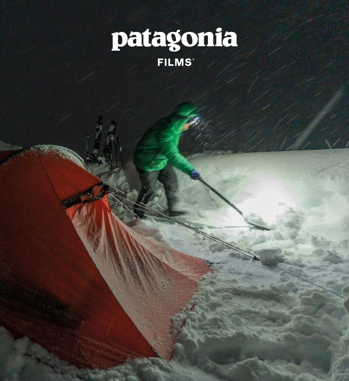 Person digging snow beside a tent in a snowy nighttime storm