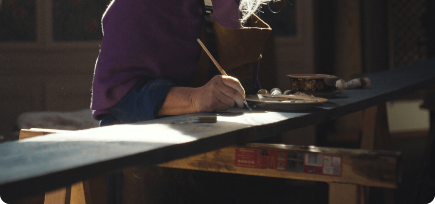 Anati Graetz carefully painting skis by hand at a workbench in a softly lit workshop.