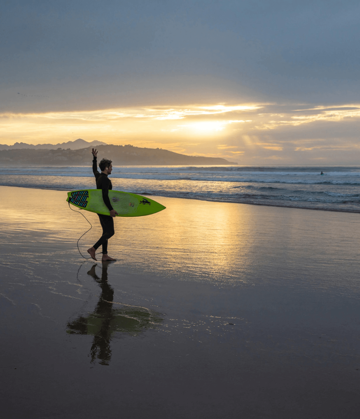 Surfer walking along the beach at sunset holding a bright yellow board