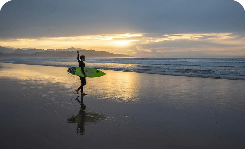 Surfer walking along the beach at sunset