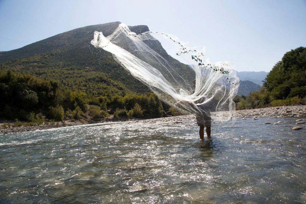 A person pulls discarded clothes from a trash pile in the desert. 
